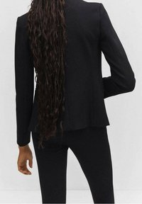 Blazer noir cintré avec manches longues, épaules structurées et légère évasement à l'ourlet. Porte avec un pantalon noir assorti.