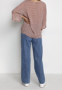 Blouse rouge à motifs avec des manches trois-quarts et un trou de clé à l'arrière, associée à un jean large bleu clair et des baskets blanches.