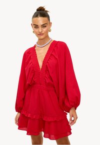 Robe rouge à manches longues, avec un col et un ourlet froncés, une taille élastique et une jupe à plusieurs couches. Tissu doux avec une texture lisse.