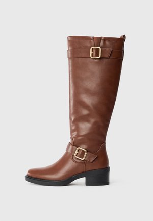 Brown knee-high leather boot with two gold buckles, low black block heel, and pull tab at the back on a plain white background.