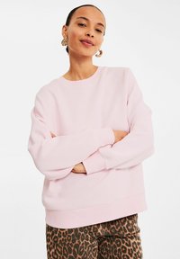 Helles pinkes Sweatshirt mit Rundhalsausschnitt, weiten Ärmeln und gerippten Bündchen, kombiniert mit braunen Leopardmuster-Hosen. Glatte Stofftextur.