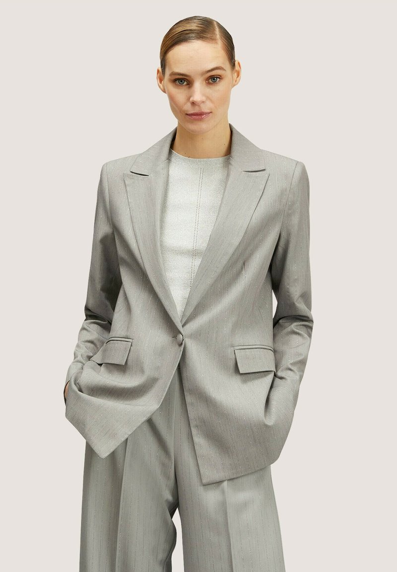Blazer grigio chiaro in tessuto texture, con colletto a rever, due tasche frontali e chiusura con un solo bottone. Abbinato a pantaloni a gamba larga coordinati.