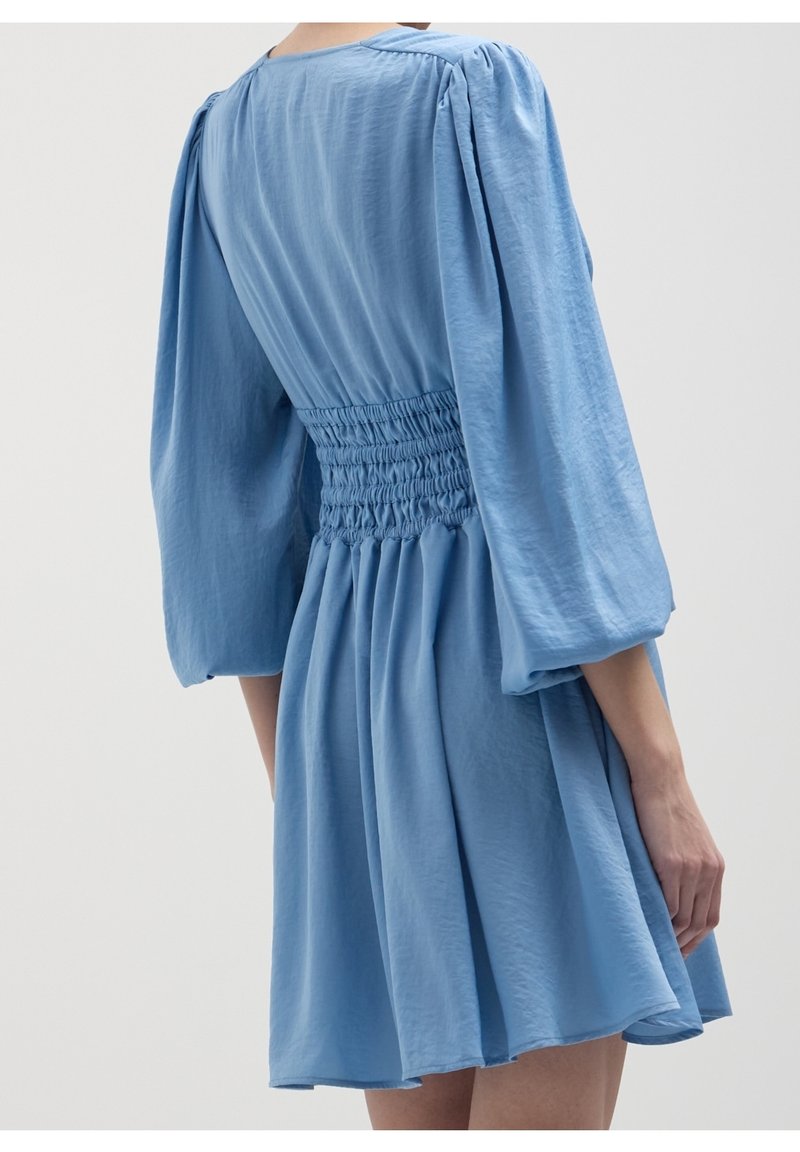 Robe bleu clair avec une texture lisse, des manches bouffantes et une taille froncée, dotée d'une jupe évasée arrivant à mi-cuisse.