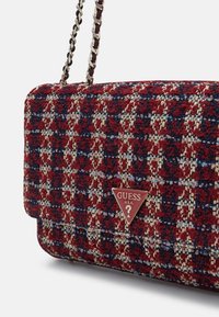 Red and navy patterned tweed crossbody bag with gold chain strap and triangular metal logo plate, featuring a quilted texture and flap closure.