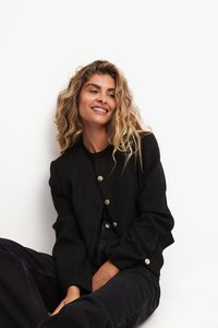 Must mustriga tehtud jakk, millel on sobiv disain, ümmargune krae ja kaks kuldset nuputugevust ees. Kantud musta sisa ja tumedate pükstega.