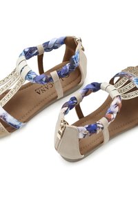 Beige Sandalen mit geflochtenen blauen und weißen Riemen, dekorativen goldenen Akzenten und einem Reißverschluss auf der Rückseite. Braune Innensohle; flacher Absatz.