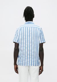 Īsroku krekls gaiši zilās un baltās svītrās, izgatavots no teksturētas auduma ar klassisku apkakli un taisnu apakšu.