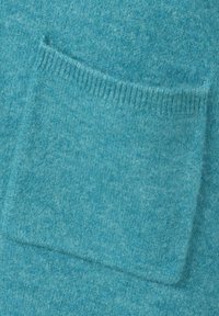 Nahaufnahme eines weichen blauen Strickstoffs mit einer rechteckigen Tasche, die oben mit Rippkante versehen ist.