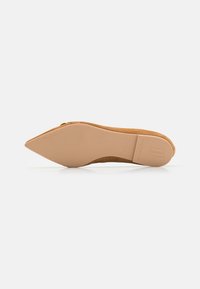 Chaussure plate nude en daim à bout pointu avec un talon fin et effilé. Texture extérieure lisse, semelle flexible et logo embossé au dos.