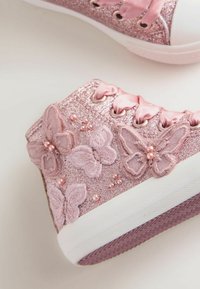 Różowe, błyszczące sneakersy za kostkę z wyszywanymi akcentami motyli, satynowymi sznurowadłami i perłowymi detalami na fakturowanej białej podeszwie.