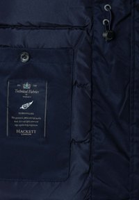 Chaqueta azul marino rellena de plumón con una textura suave, que cuenta con un bolsillo con una etiqueta de logotipo y un ajuste de cordón cerca del cuello.