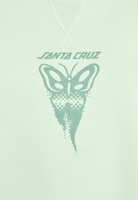 A menta zöld anyagon stilizált pillangó grafika látható sötétzöld színben, a dizájn felett pedig a "SANTA CRUZ" felirat olvasható.