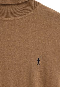 Brun polotröja av stickad tyg, med ribbad krage och en liten svart logotyp på bröstet, slät textur.