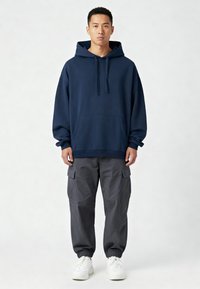 Felpa blu navy con tasca frontale e cordino, abbinata a pantaloni cargo grigi con polsini elastici e tasche laterali, indossata con sneakers bianche.