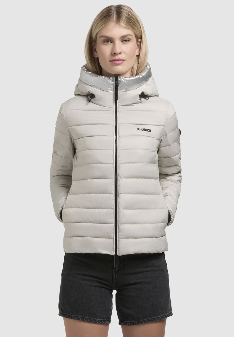 Lichtgrijze pufferjack met een glanzende capuchon, ritssluiting aan de voorkant en zwarte koordjes. Voorzien van horizontale quiltstrepen en een geborduurd logo op de borst.