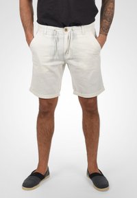 Pantalones cortos de hombre en un tono beige claro, con un corte relajado, cierre con cordón, dobladillos enrollados, bolsillos laterales y una tela texturizada.
