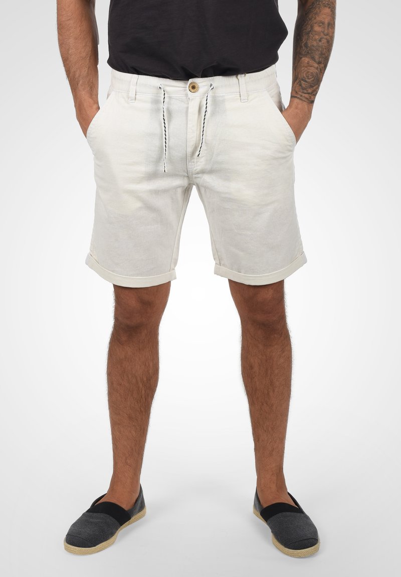Pantalones cortos de hombre en un tono beige claro, con un corte relajado, cierre con cordón, dobladillos enrollados, bolsillos laterales y una tela texturizada.