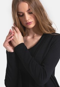 Czarna, prążkowana bluzka z długim rękawem i dekoltem w kształcie V. Posiada teksturowany materiał i dopasowany krój, podkreślający rękawy oraz subtelne drapowania.