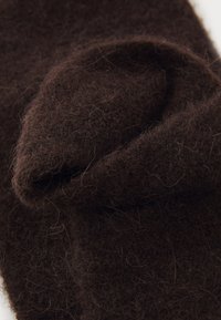 Lana infeltrita marrone, texture morbida, leggermente stropicciata con fibre visibili. Il materiale ha un colore caldo e ricco e un aspetto accogliente.
