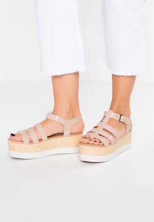 Beige platform sandalen met meerdere banden, een dikke houten zool en een witte rubberen basis; voorzien van een gespsluiting op de enkelband.