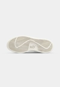 Semelle d'une basket blanche Puma avec motif en chevrons et logo Puma au centre sur un fond clair uni.