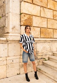 Jersey a rayas en blanco y negro con cuello, que presenta el logo de "ARISTON" y la bandera italiana. Combinado con pantalones cortos de mezclilla y botas negras hasta el tobillo.