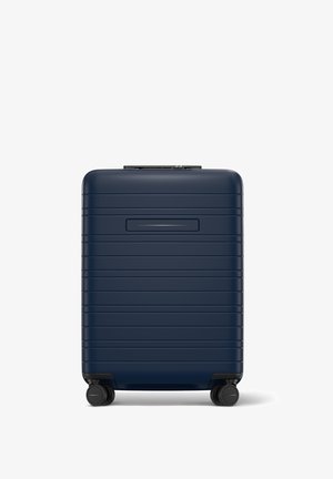 Valise rigide bleu marine avec une surface striée, poignée rétractable et quatre roues noires pour une mobilité facile.