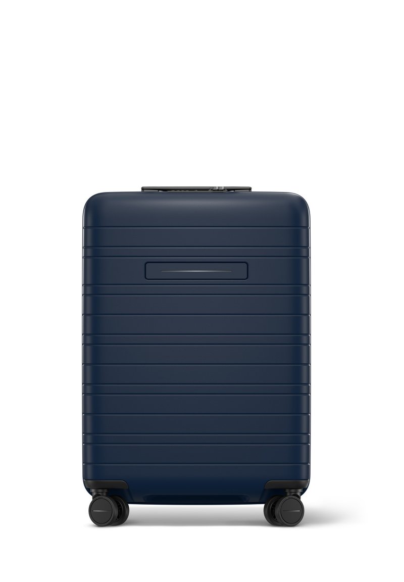 Valise rigide bleu marine avec une surface striée, poignée rétractable et quatre roues noires pour une mobilité facile.