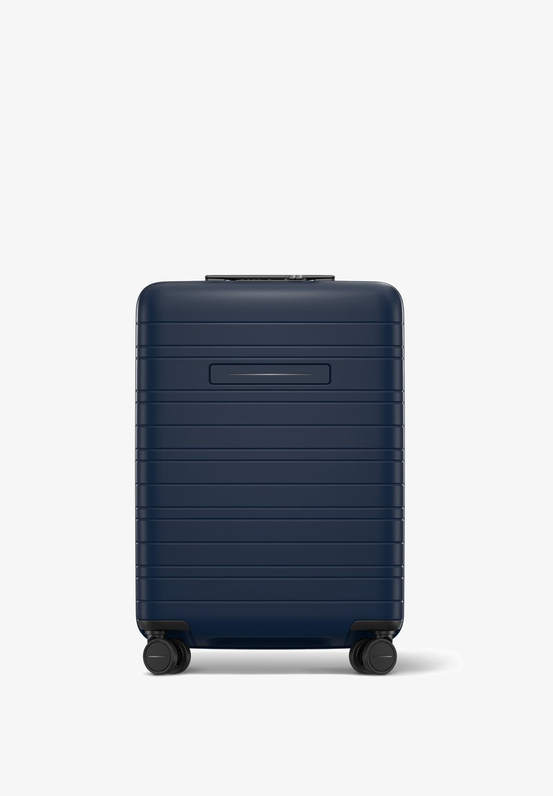 Valise rigide bleu marine avec une surface striée, poignée rétractable et quatre roues noires pour une mobilité facile.