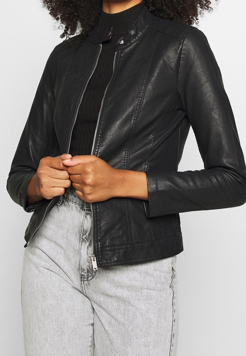 Black leather jacket with a stand-up collar, zip closure, and fitted design. Paired with high-waisted light gray jeans.