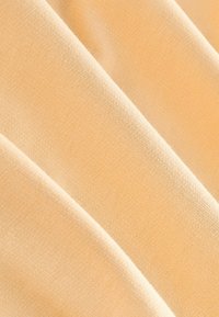Peach-colored fabric with a smooth texture, featuring a finely woven pattern. The material appears soft and pliable, with draped folds.