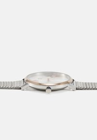 Montre avec bracelet en maille argentée, cadran rond blanc, accents en or rose et couronne sertie de saphirs. Comprend des index d'heure clairs.