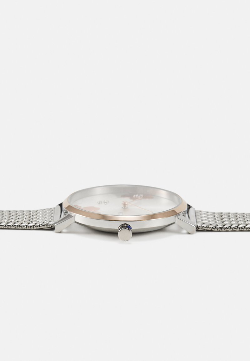 Silbernes Mesh-Armband-Uhr mit einem runden weißen Zifferblatt, roségoldenen Akzenten und einer mit Saphiren besetzten Krone. Enthält klare Stundenmarker.