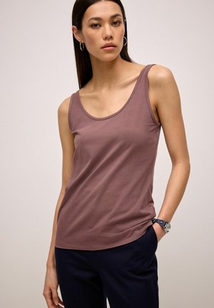 Lyserød tanktop lavet af blødt stof, med en rund halsudskæring og smalle stropper. Mixet med mørk navy bukser og et armbåndsur.