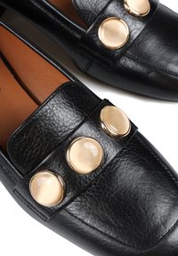 Czarne skórzane mokasyny charakteryzują się gładką teksturą, trzema dużymi przezroczystymi guzikami z złotymi akcentami oraz beżowym wnętrzem.