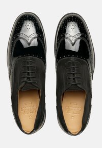 Schwarze Lederschuhe mit polierter Oberfläche, die über Brogue-Verzierungen und eine Kombination aus glatten und Wildledertexturen verfügen.