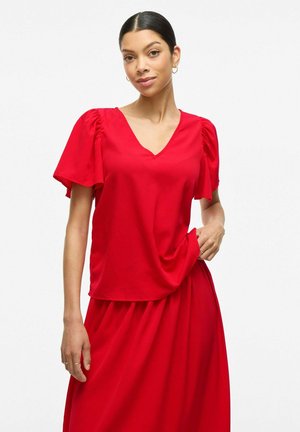 Red short-sleeve top with a V-neck, featuring puffed sleeves. Made of smooth fabric, loosely draping over the body, paired with a matching skirt.
