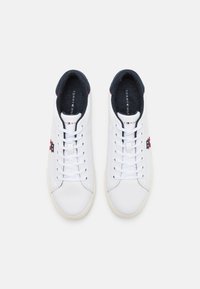 Zapatillas de cuero blancas con una textura suave, con forro azul marino, cordones blancos y un logo rojo y azul en el lateral.