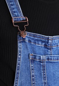 Jeansoverall i blekblått, med kopparfästen, justerbara axelremmar och framfickor med kontrasterande sömmar. Texturerad svart ribbad tröja under.