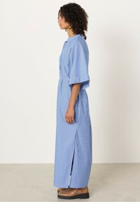 Abito a strisce blu e bianche, a maniche lunghe, con colletto, cintura in vita e spacchi laterali. Realizzato in tessuto leggero con una texture liscia.