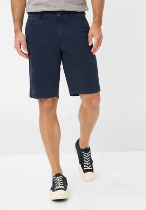 Marineblauwe shorts van katoen met een rechte voorkant, zijzakken en riemlussen, gecombineerd met marineblauwe canvas sneakers met crèmekleurige veters.