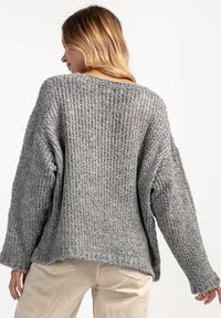 Szary, teksturowany sweter z dzianiny o luźnym, oversize'owym kroju, z obniżonymi ramionami i szerokim dekoltem. Dół jest nieco dłuższy z tyłu.