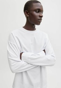 Hvid langærmet skjorte med rund halsudskæring og afslappet pasform. Blødt bomuldsstof med subtil struktur. Arme krydset.