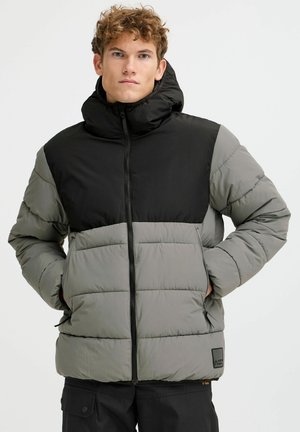 Chaqueta puffy negra y gris con un cuello alto, cremallera frontal y dos bolsillos laterales; presenta textura acolchada y logo bordado en el dobladillo.