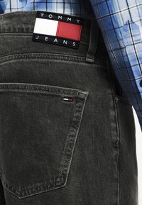 Μαύρο τζιν παντελόνι με ετικέτα Tommy Jeans στο πίσω μέρος, με κόκκινες, λευκές και μπλε λεπτομέρειες, και ελαφρώς υφασμένο ύφασμα.