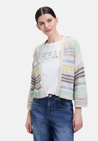 Strickjacke mit mehrfarbigen Streifen in sanften Pastellfarben, lockere Passform und Dreiviertelärmel. Getragen über einem weißen T-Shirt.