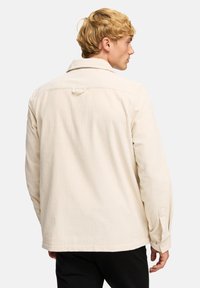 Giacca in corduroy beige con colletto e polsini abbottonati, che mostra una texture a coste verticali e un asola sul retro.