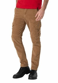 Bruine corduroy cargo-broek met meerdere zijzakken, taps toelopende pasvorm en een zachte textuur, gecombineerd met zwarte veterschoenen.