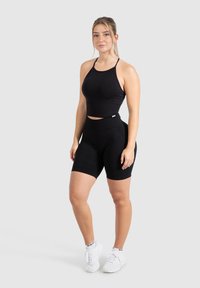 Zwart sportief crop top en high-waisted fietsbroek gemaakt van rekbare stof. Heeft dunne banden en een naadloos ontwerp, gecombineerd met witte sneakers.