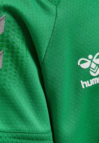 Groene sportshirt van een textuurstof, met een logo van een honingbij en een merknaam in het wit. Het ontwerp bevat subtiele patroonaccenten.